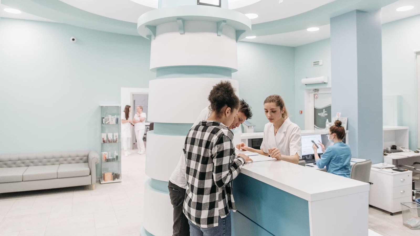 Patients check in and review paperwork with a receptionist at a modern clinic front desk.