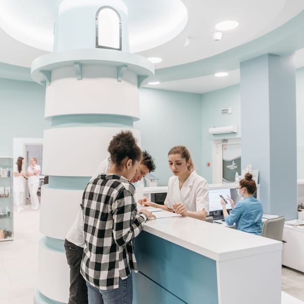 Patients check in and review paperwork with a receptionist at a modern clinic front desk.