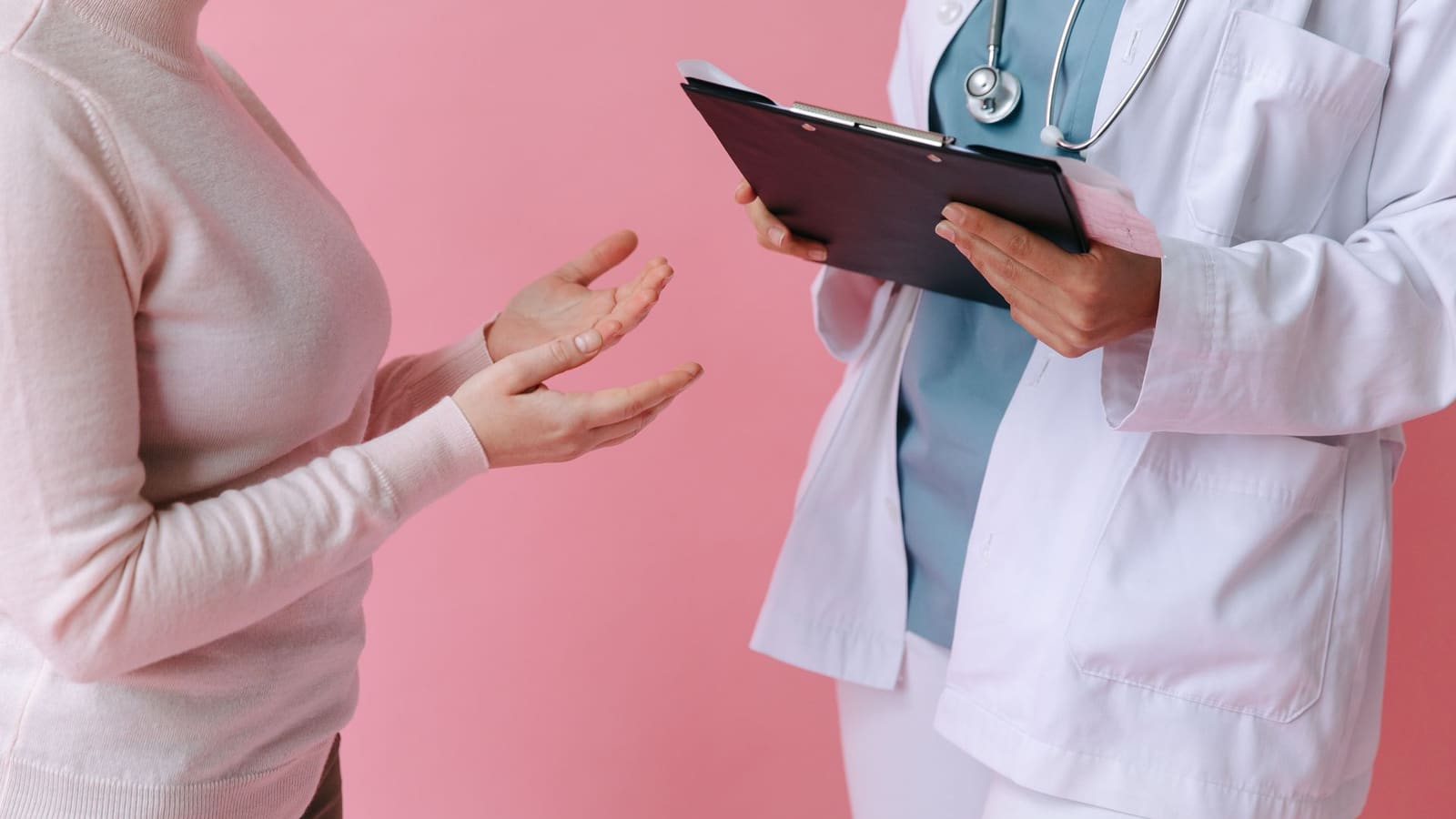 A patient describes their symptoms while a clinician with an intake clipboard listens at a first pain clinic appointment.