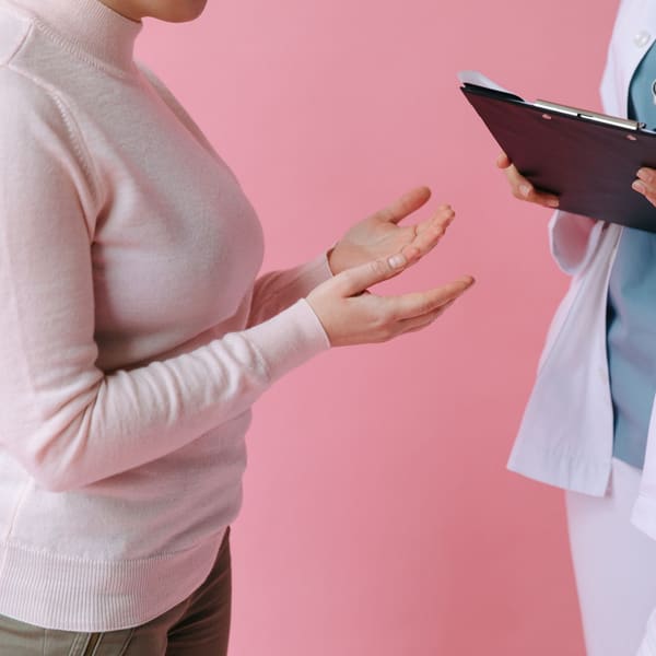 A patient describes their symptoms while a clinician with an intake clipboard listens at a first pain clinic appointment.