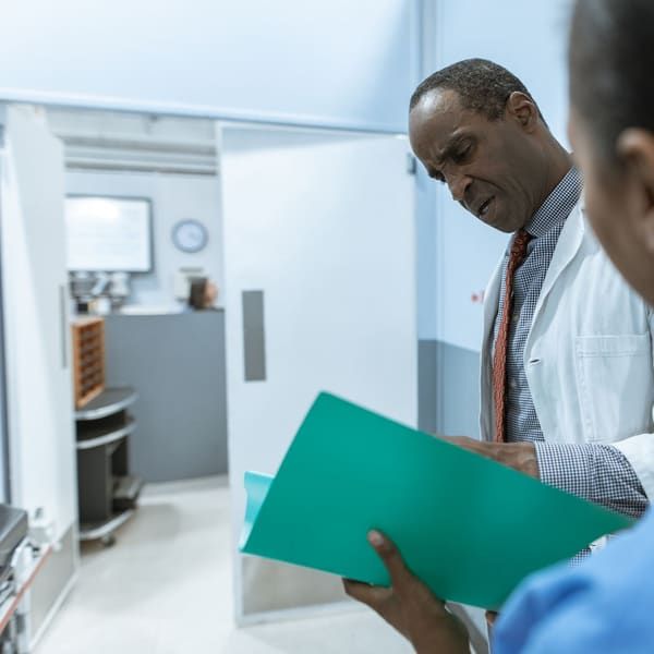 Two clinicians in a bright clinic corridor review a patient chart together in a green folder.